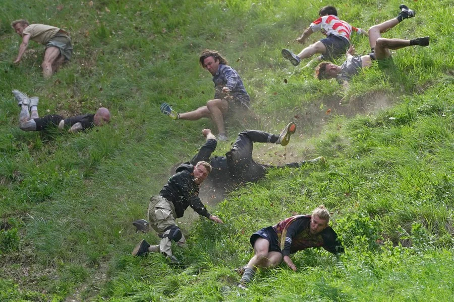 Eight men are seen tumbling and trying to run down a very steep hill. Eight men are seen tumbling and trying to run down a very steep hill.